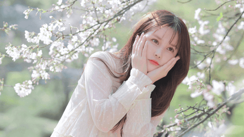 Young woman with beautiful hair smiles with cherry blossom foliage in background.